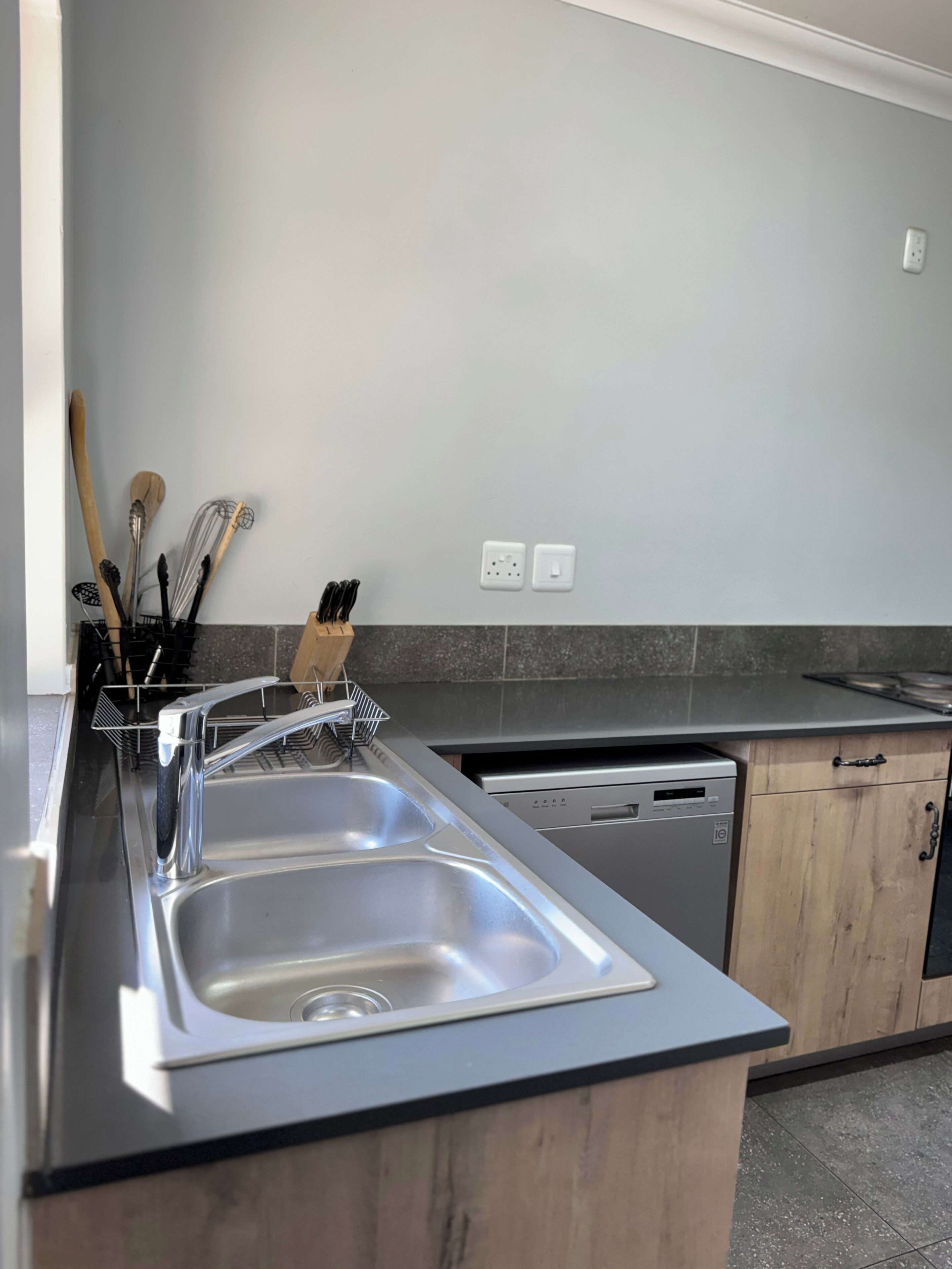 A modern kitchen with a stainless steel sink, wooden cabinets, and a dishwasher.