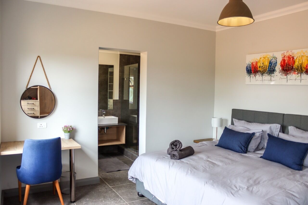 A bedroom with a bed, a desk, a chair, a mirror, and a bathroom visible through an open door.