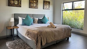 Un dormitorio moderno con una cama grande, varios almohadones, una mesita de noche con lámpara y obras de arte en las paredes.