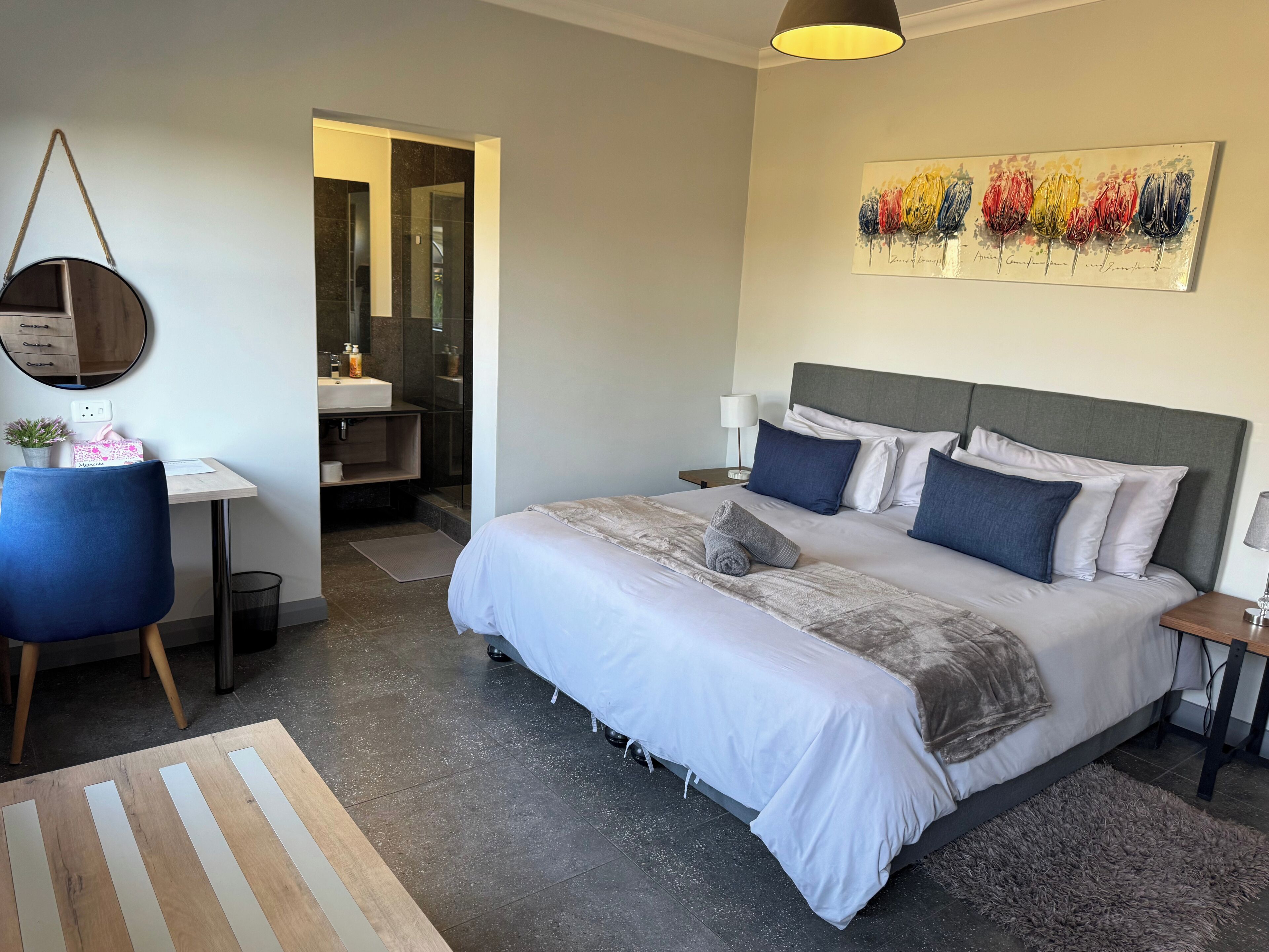 A modern bedroom with a large bed, bedside tables, a desk, and a bathroom in the background.