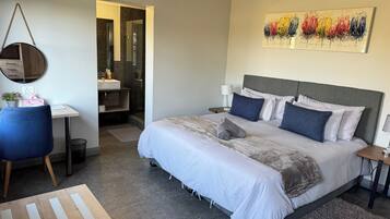 A modern bedroom with a large bed, bedside tables, a desk, and a bathroom in the background.