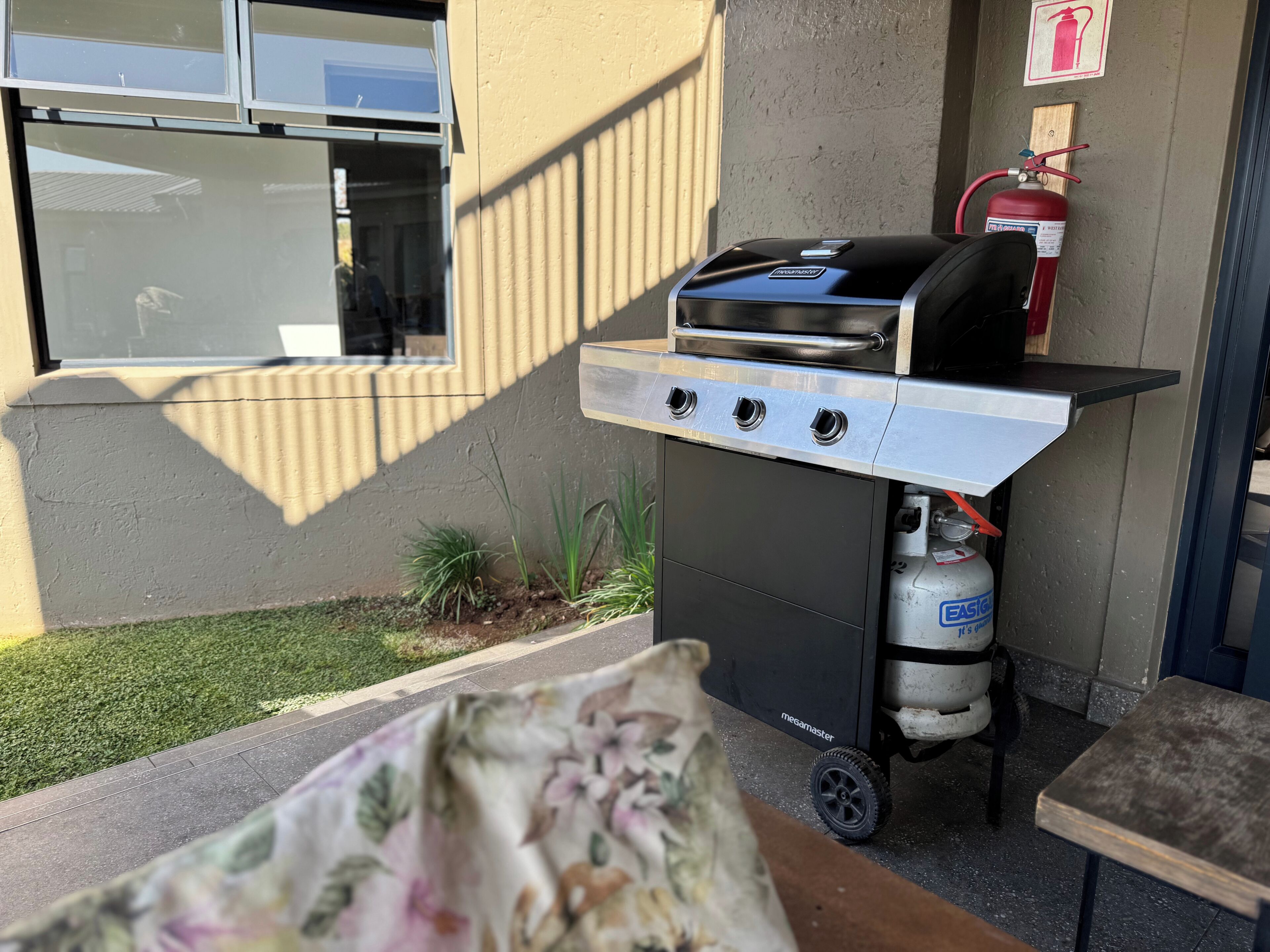An outdoor grill with a gas tank and a fire extinguisher mounted on a wall.