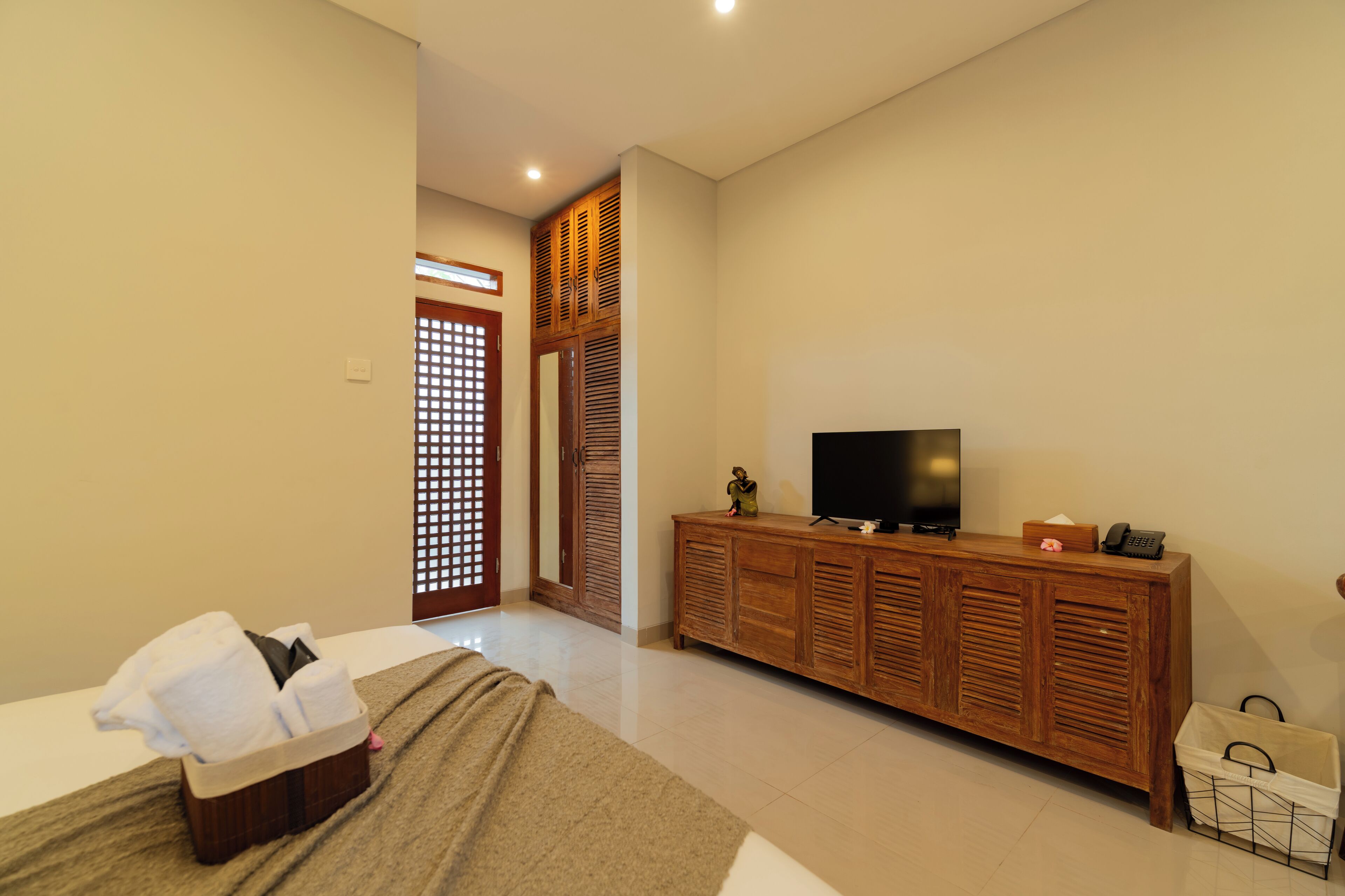 A hotel room with a bed, a wooden cabinet with a television, and a small table with a telephone and a tissue box.