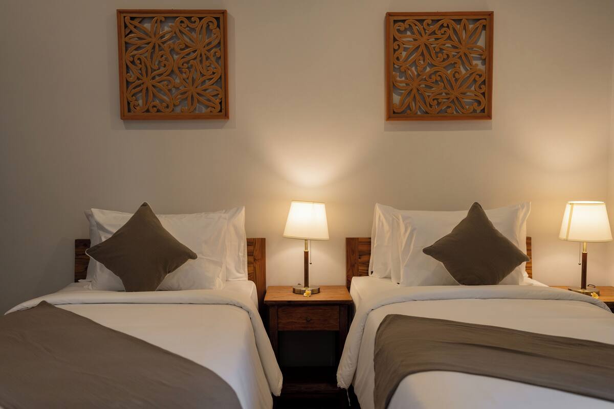 A hotel room with two beds, each with a nightstand, a lamp, and decorative wall panels.