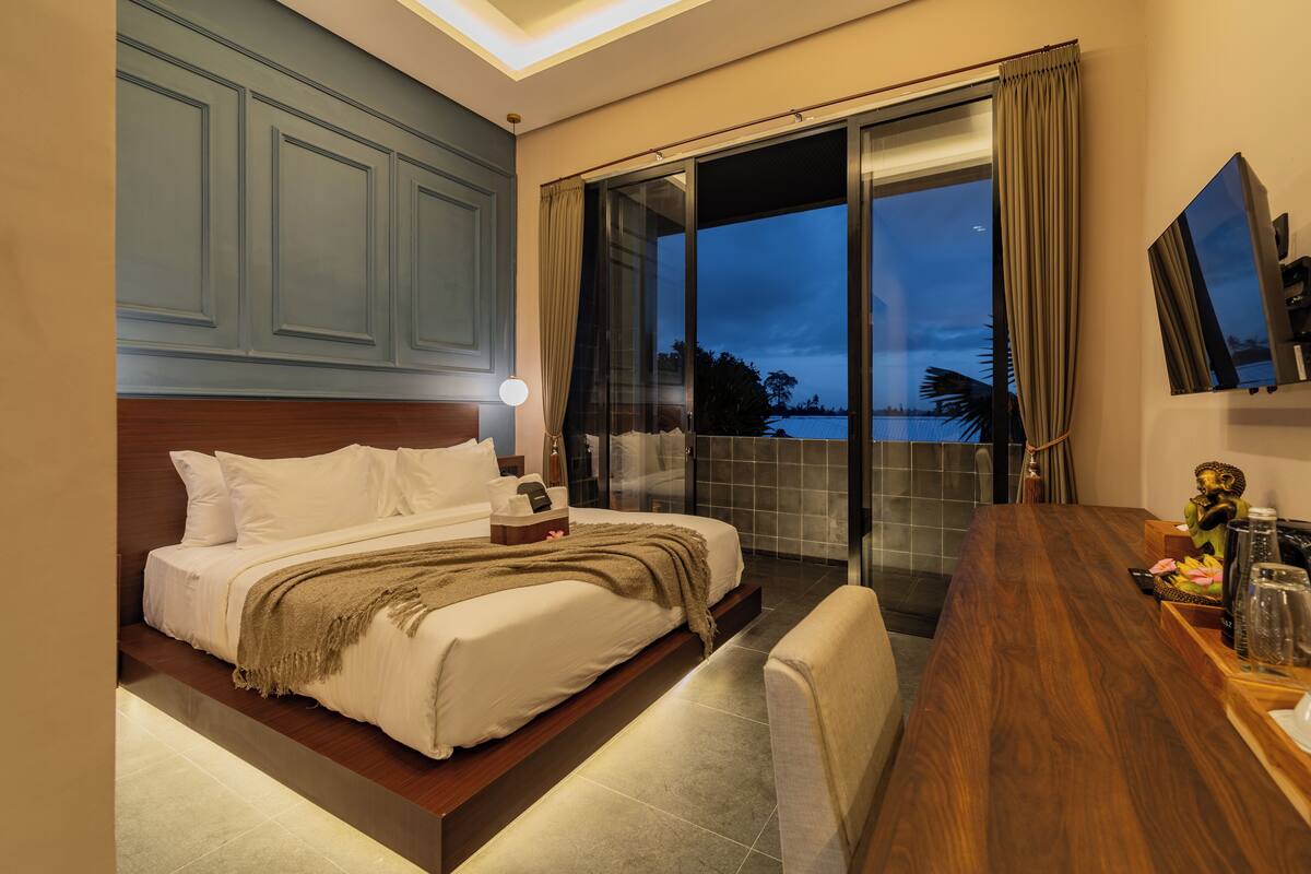 A hotel room with a bed, a desk, and a view of the outdoors.