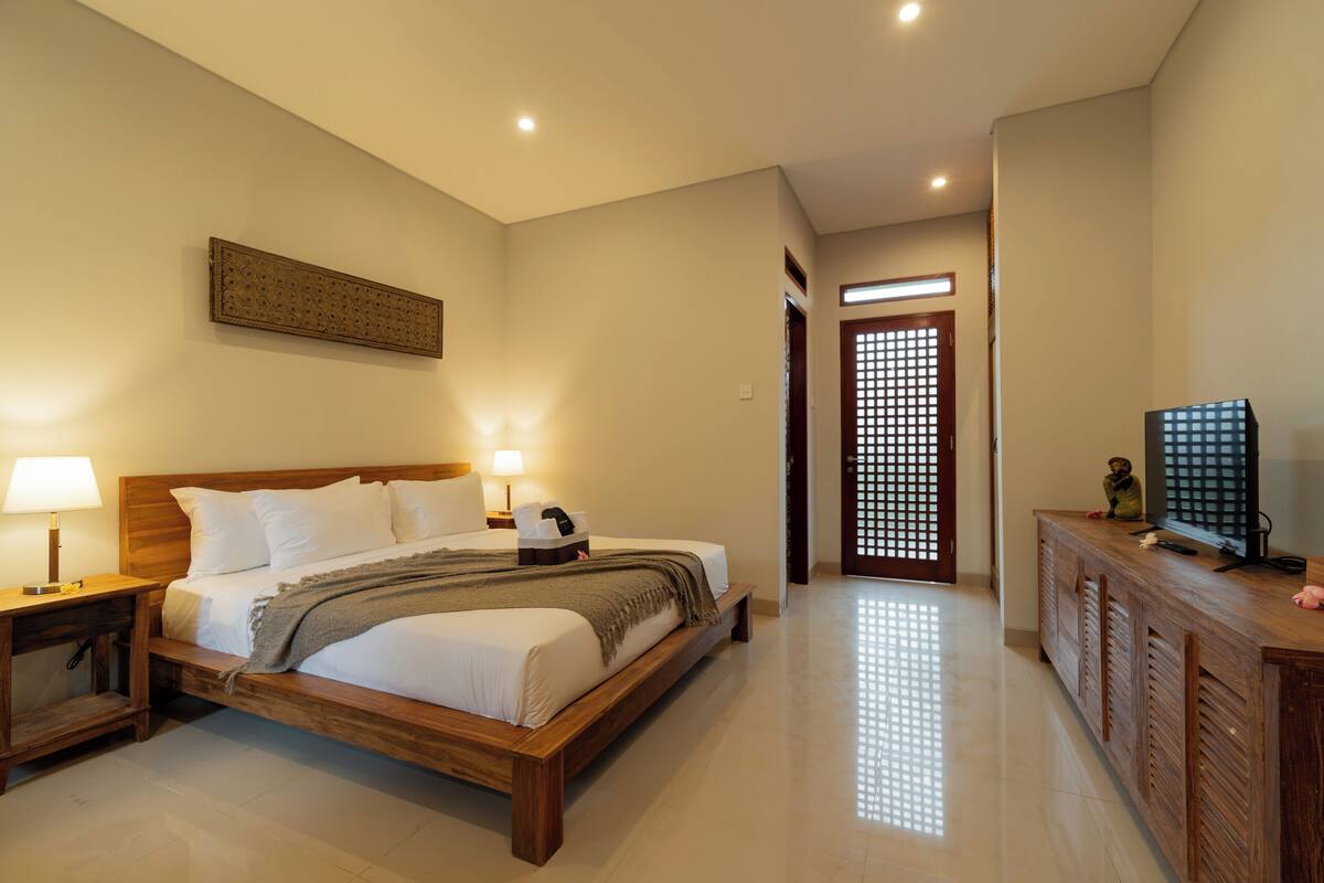 A bedroom with a wooden bed, bedside tables with lamps, a TV on a wooden cabinet, and a decorative screen door.