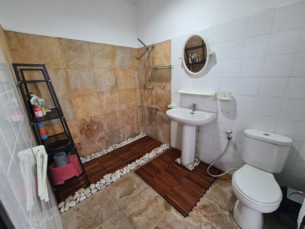 A bathroom with a shower, a sink, and a toilet. There is a shelf with toiletries and a ladder.