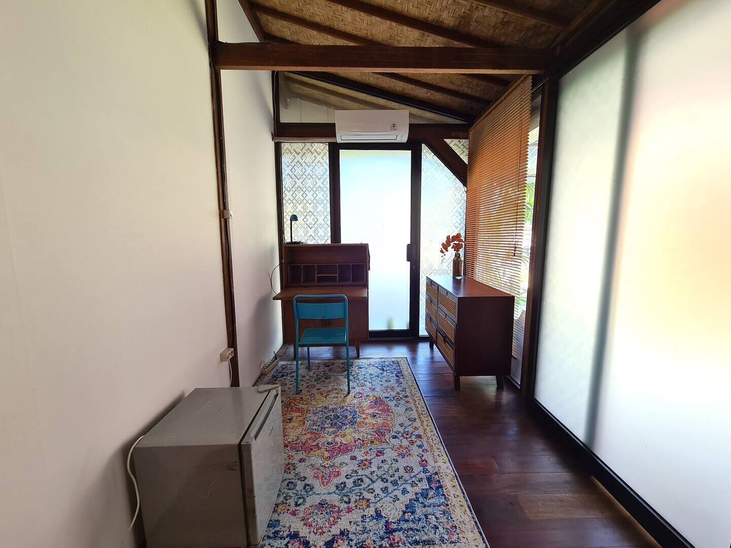 Un couloir avec un bureau en bois, une chaise bleue et un tapis à motifs.