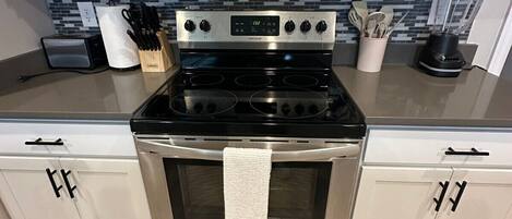 A kitchen with a stainless steel stove, oven, and microwave. There are cabinets with handles, a countertop with a toaster, and a blender.