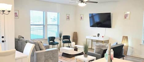 A modern living room with a flat-screen TV, a ceiling fan, and a large window.