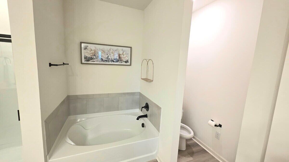 Un baño con bañera, inodoro y una obra de arte enmarcada en la pared.