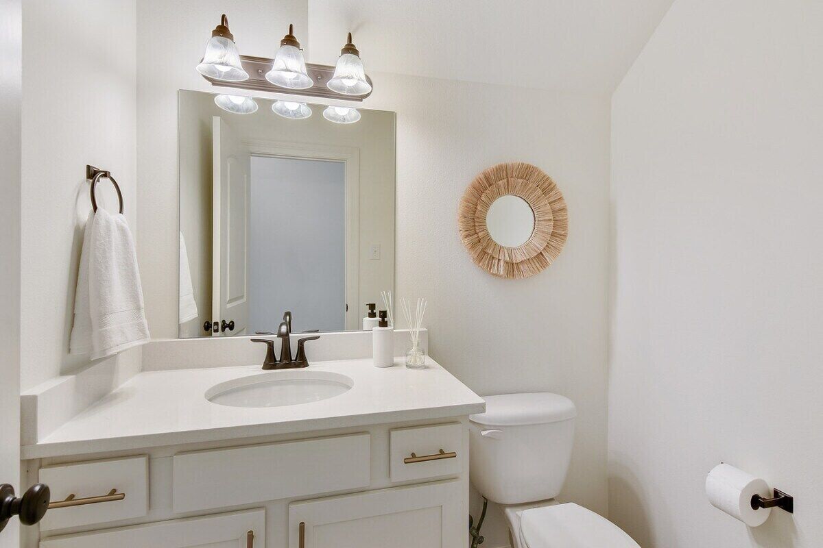 A bathroom with a white sink, a mirror, a toilet, and a wall-mounted toilet paper holder.