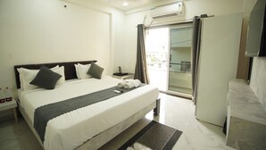 Une chambre d’hôtel avec un grand lit, une table de chevet avec une lampe, un téléviseur fixé au mur et une porte-fenêtre coulissante donnant sur un balcon.
