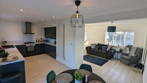 A modern kitchen with dark cabinets, a built-in oven, and a dining area with a round table and chairs. - Modern Gilliver house Rural retreat sleeps 7 (Newbold Verdon)