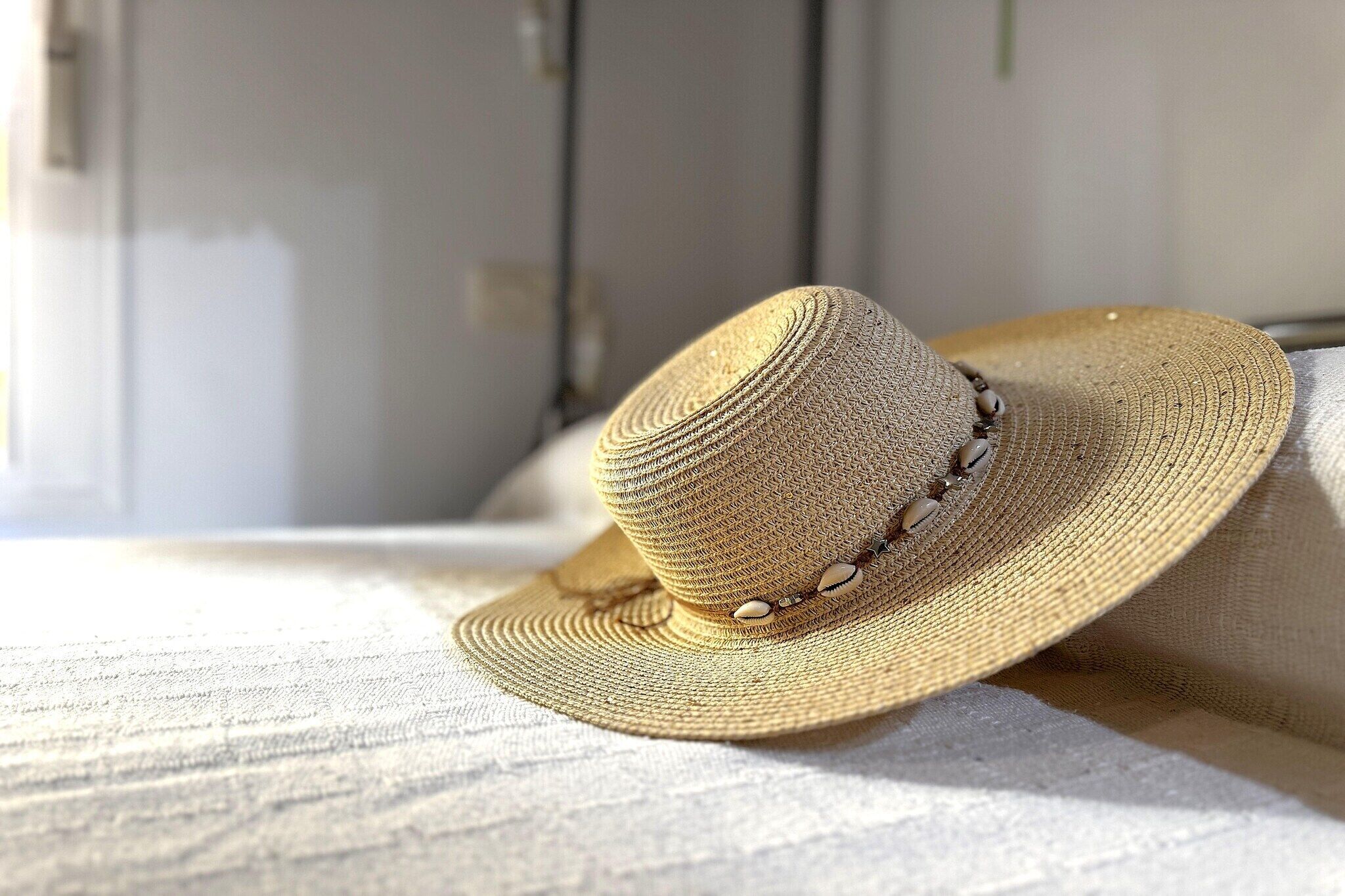 Un sombrero de paja con una banda de cuentas, sobre una superficie de tela con textura.