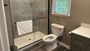 Een badkamer met een douche met glazen wand, een toilet en een wastafel met lades.