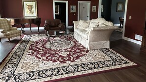 Una sala de estar con un tapete grande estampado, un sofá color beige, un sillón marrón y una mesa de centro de vidrio.