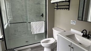Un baño con cabina de ducha de vidrio, inodoro, lavamanos y perchero para toallas.