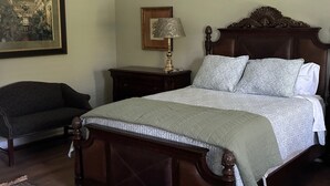 Un dormitorio con una cama grande, una mesita de noche con lámpara, un sofá oscuro y un cuadro enmarcado en la pared.