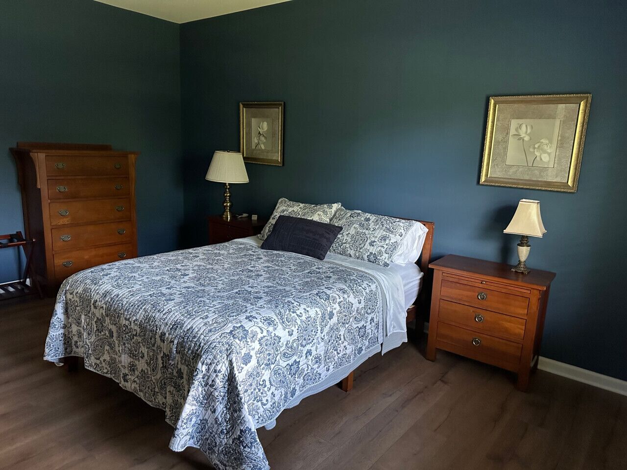 A bedroom with a bed, two nightstands, a dresser, and framed pictures on the wall.