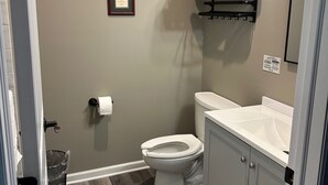 Une salle de bain avec des toilettes, un lavabo et un miroir. Un certificat encadré est accroché au mur, et un porte-serviettes se trouve au-dessus des toilettes.