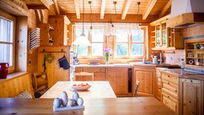 Interior de una cabaña de madera con cocina, comedor y ventanas amplias.