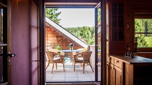 Puerta abierta a un cuarto con interior de madera, una mesa de comedor con sillas y vistas a un paisaje verde.