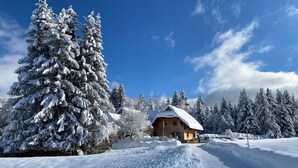 Un paisaje nevado con una cabaña de madera, árboles cubiertos de nieve y un cielo azul despejado.