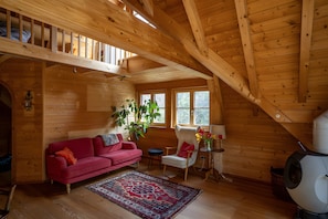 Ein Holzblock-Interieur mit einem roten Sofa, einem weißen Sessel, einem Teppich und einem großen Fenster.