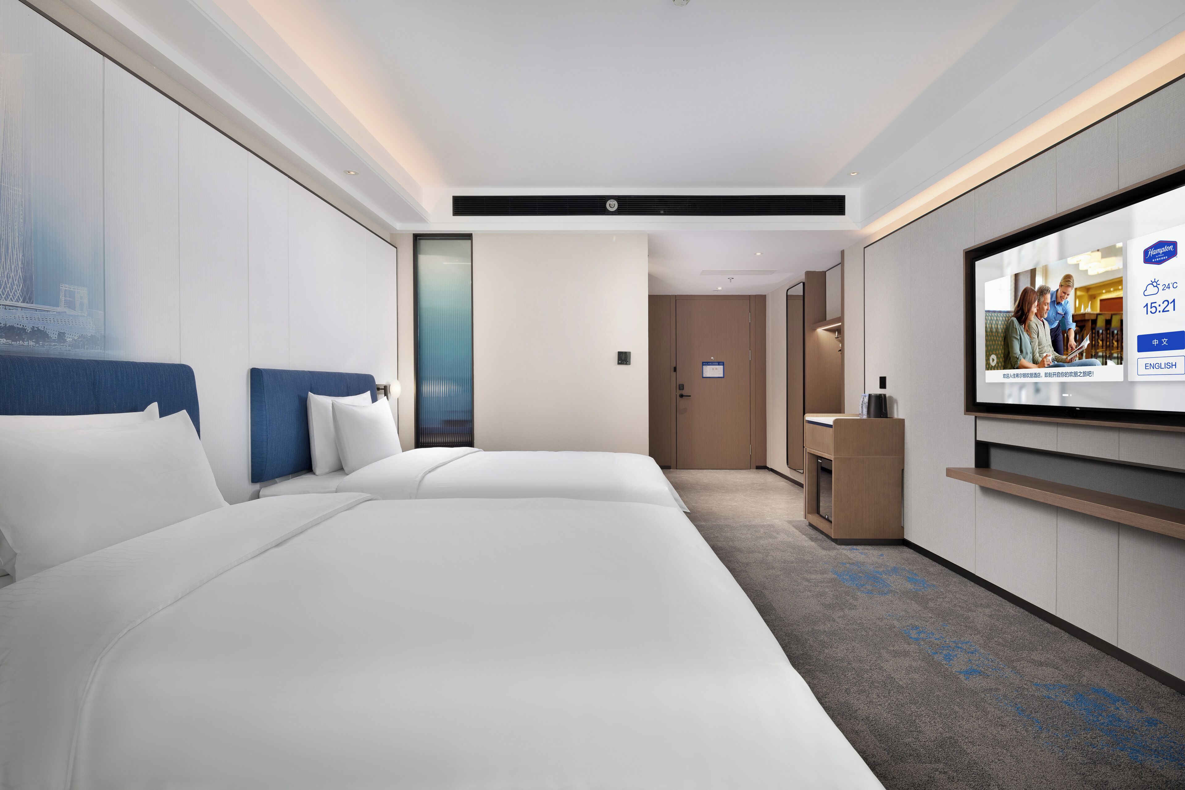 A hotel room with two beds, a TV, a desk, and a view of a cityscape.
