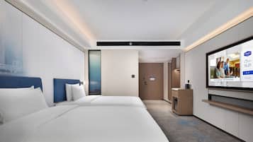 A hotel room with two beds, a TV, a desk, and a view of a cityscape.