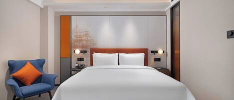 A hotel room with a large bed, a chair, a nightstand, and a wall-mounted lamp.