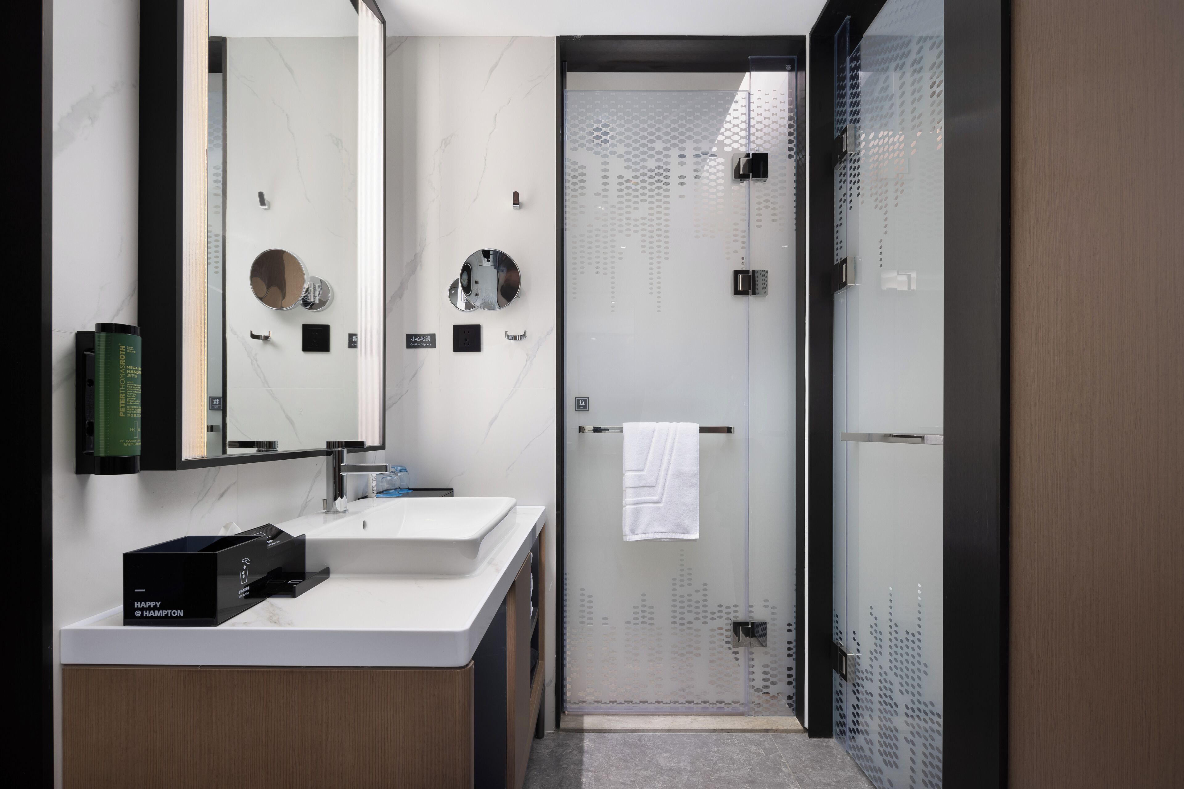 A modern bathroom with a large mirror, a white sink, and a glass-enclosed shower.