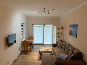 Een woonkamer met een bank, een tafel, een aan de muur bevestigde televisie en een schuifdeur die uitkomt op een balkon.