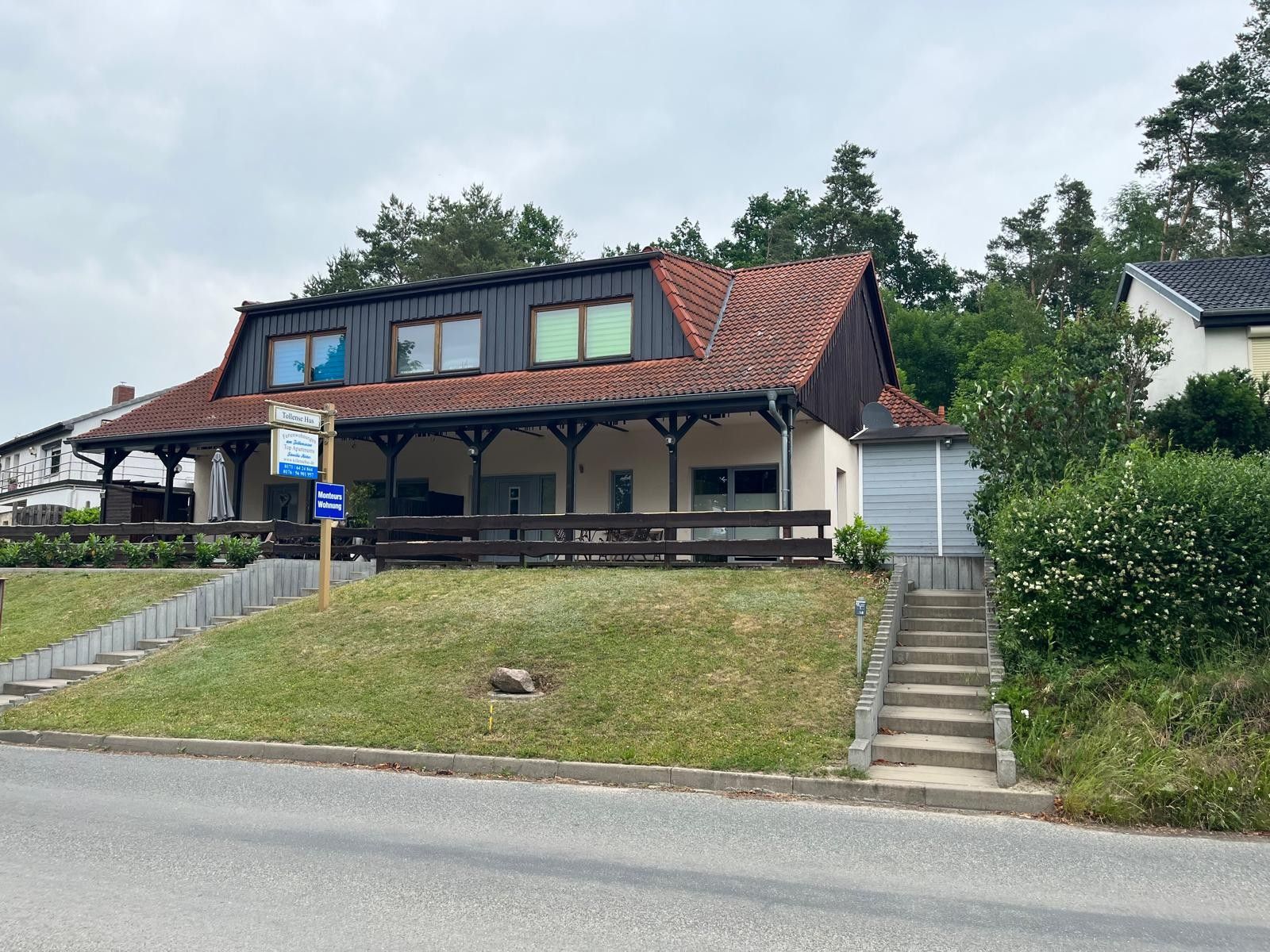 Een gebouw met twee verdiepingen, een overdekte veranda, een bordje dat een restaurant aangeeft, en een trap naar de ingang.