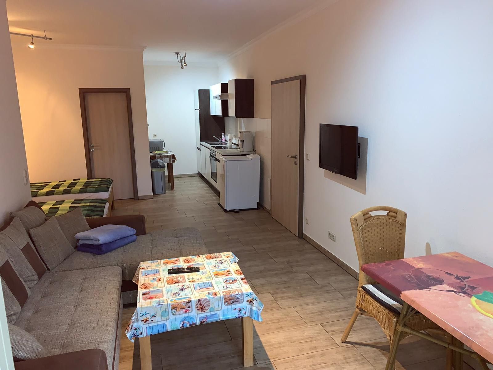 Un espacio habitable compacto con un sofá, una mesita, una mesa de comedor, una zona de cocina y un televisor montado en la pared.
