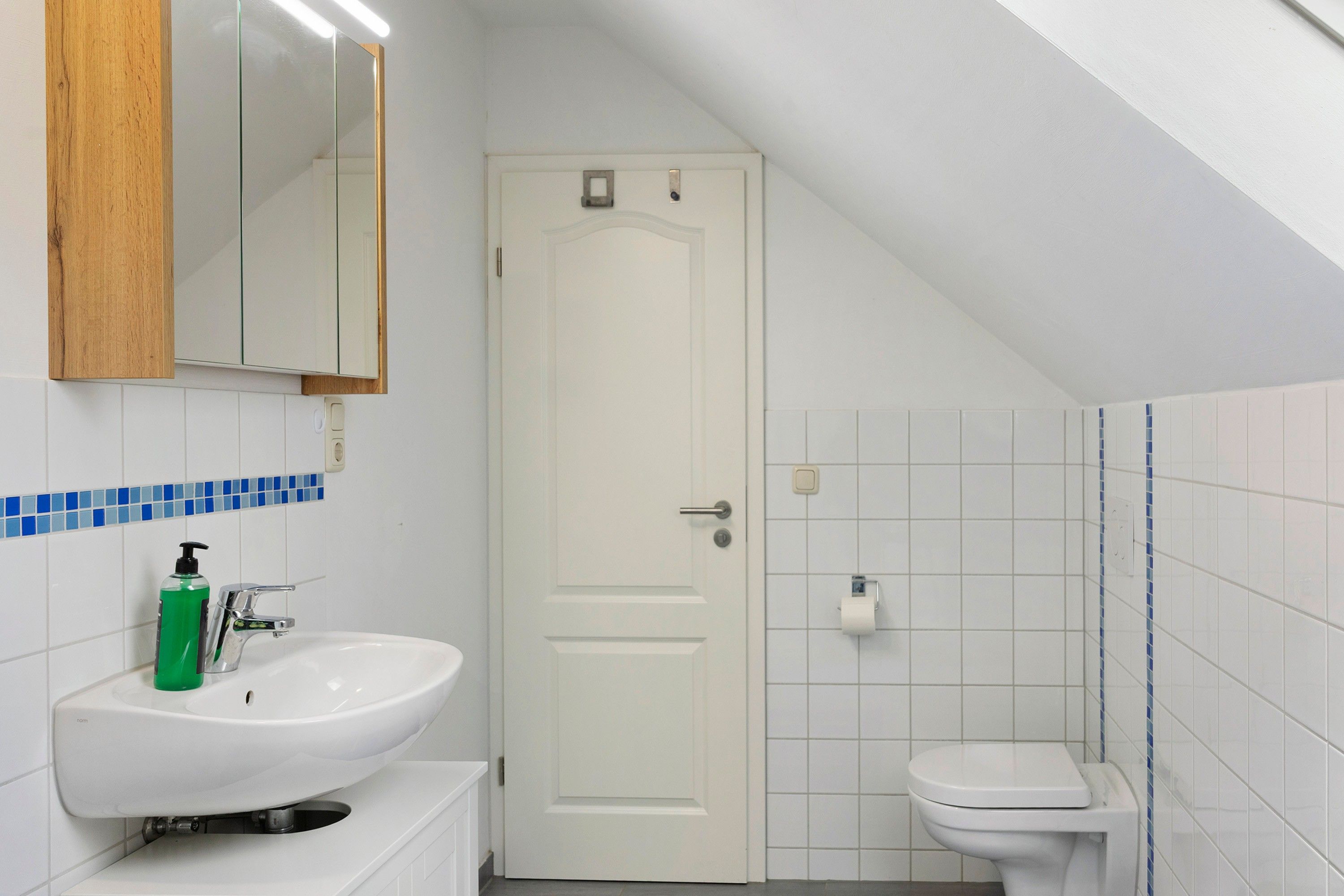 A bathroom with a white sink, a mirror, a toilet, and a door.