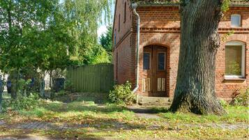 A brick building with a large tree in front, a wooden fence, and a paved driveway.