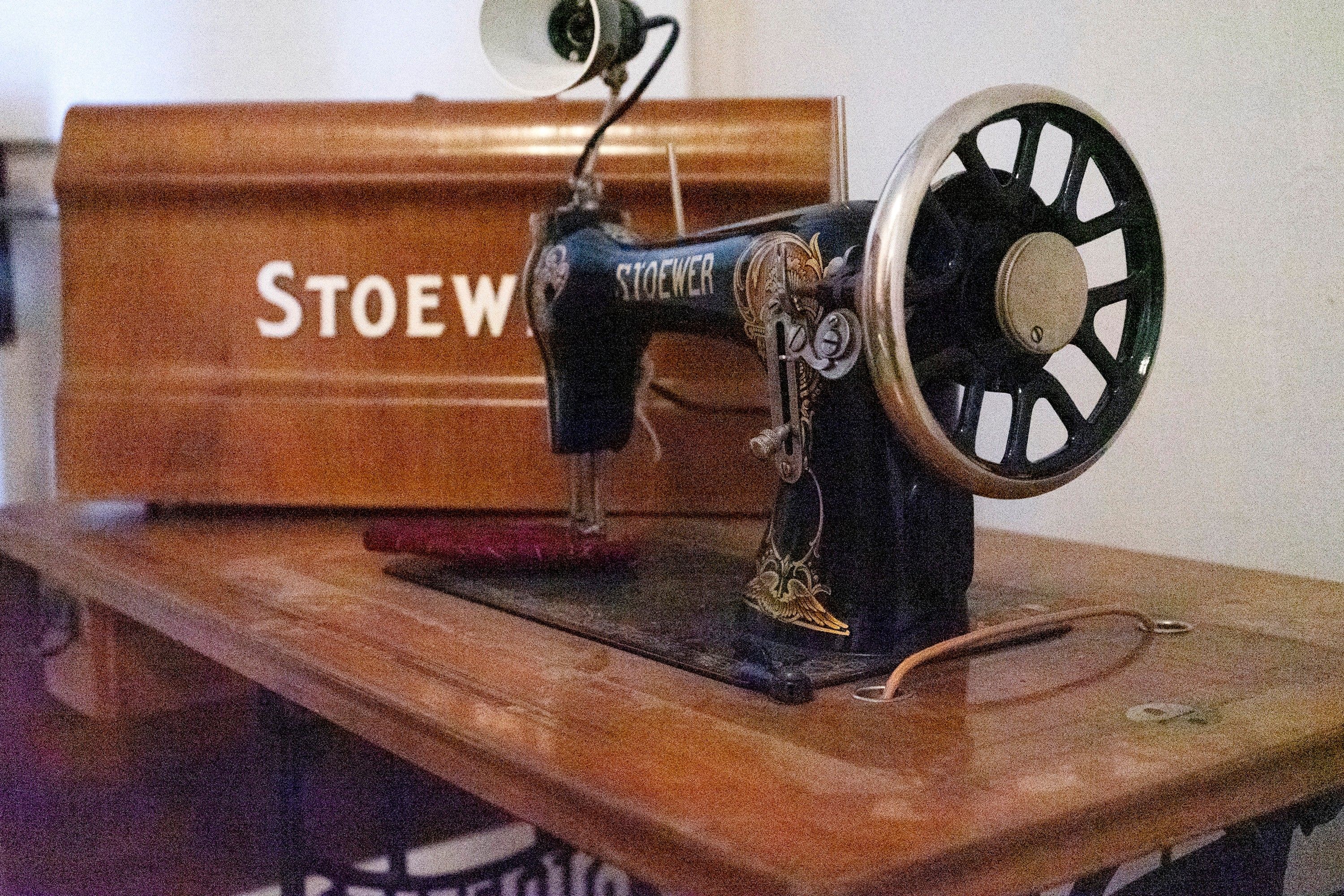 A vintage sewing machine on a wooden table with a wooden box labeled 'STOEW' in the background.