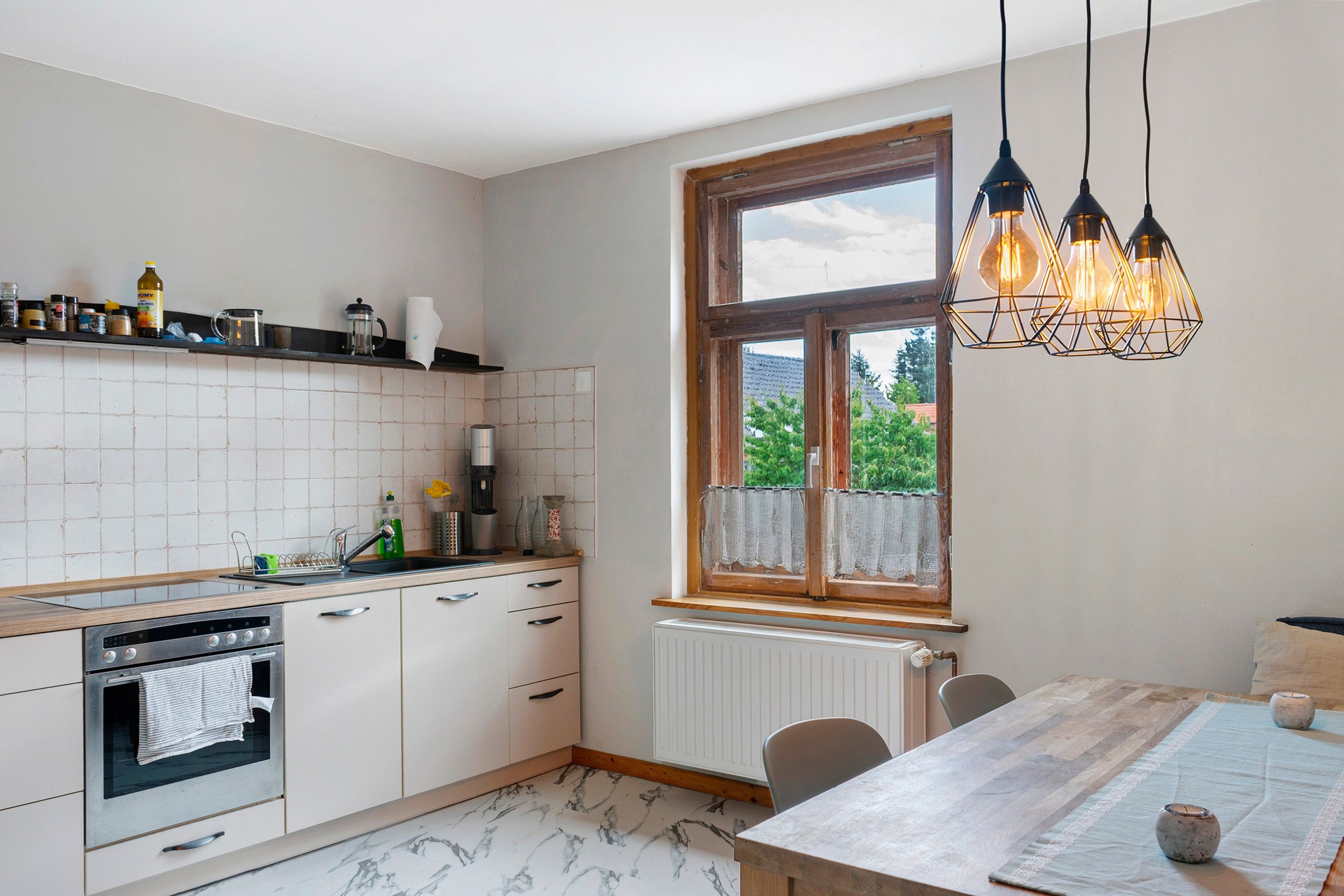 Cocina moderna con armarios blancos, horno empotrado, ventana con vistas e iluminación colgante.