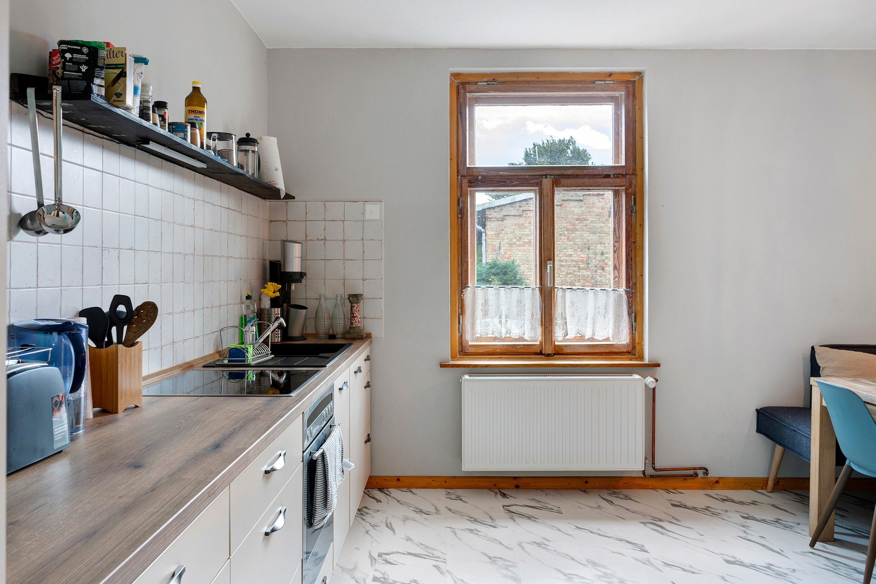Une cuisine avec une fenêtre, des carreaux blancs, un plan de travail en bois et un radiateur.