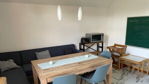 A room with a wooden table, blue chairs, a dark sofa, a small TV, and a chalkboard.