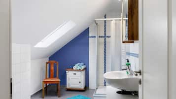 A narrow bathroom with a skylight, a wooden chair, a small cabinet, and a sink with a mirror.