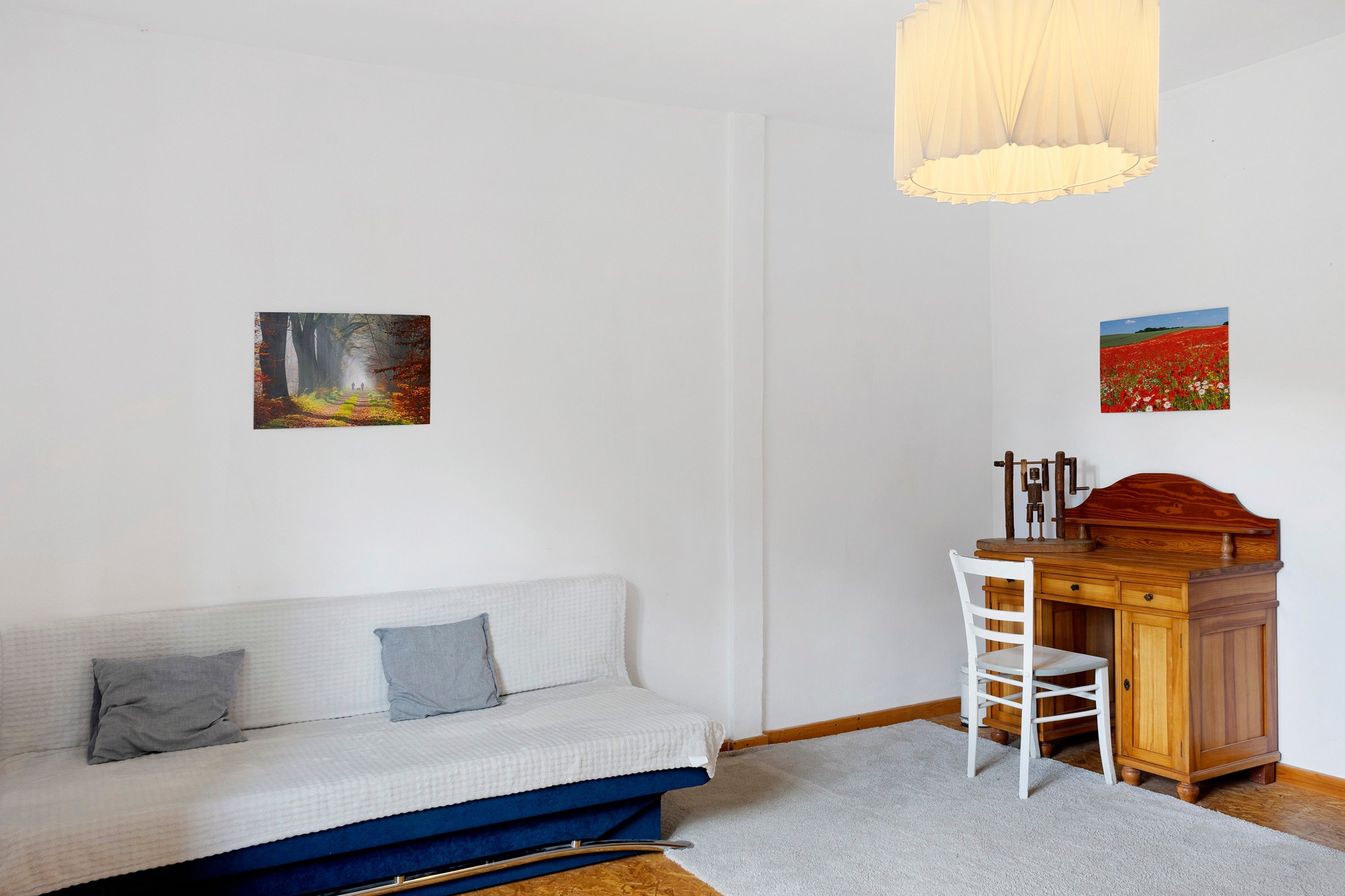 Una habitación con sofá, un escritorio con silla y dos cuadros en la pared.