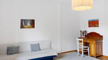 Una habitación con sofá, un escritorio con silla y dos cuadros en la pared.