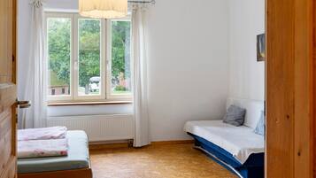 Ein kleines Zimmer mit Fenster, Heizkörper, Bett und Holztür.