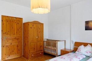 A bedroom with a wooden wardrobe, a crib, a bed with floral bedding, and a wall-mounted picture. - Holiday Apartment 'Pieck' with Shared Garden and Wi-Fi (Raduhn)