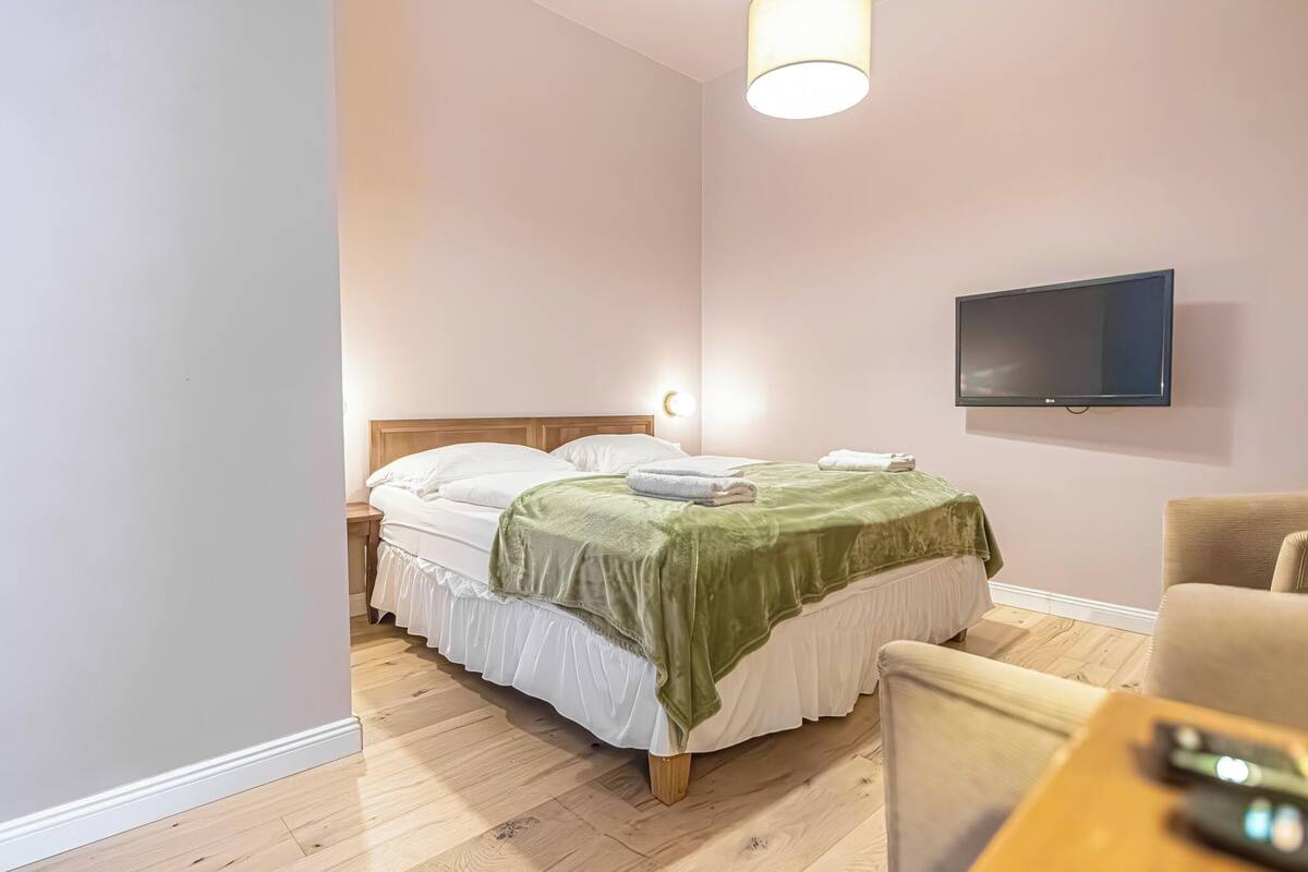 A neatly arranged bedroom with a bed, bedside tables, a TV, and a chair.