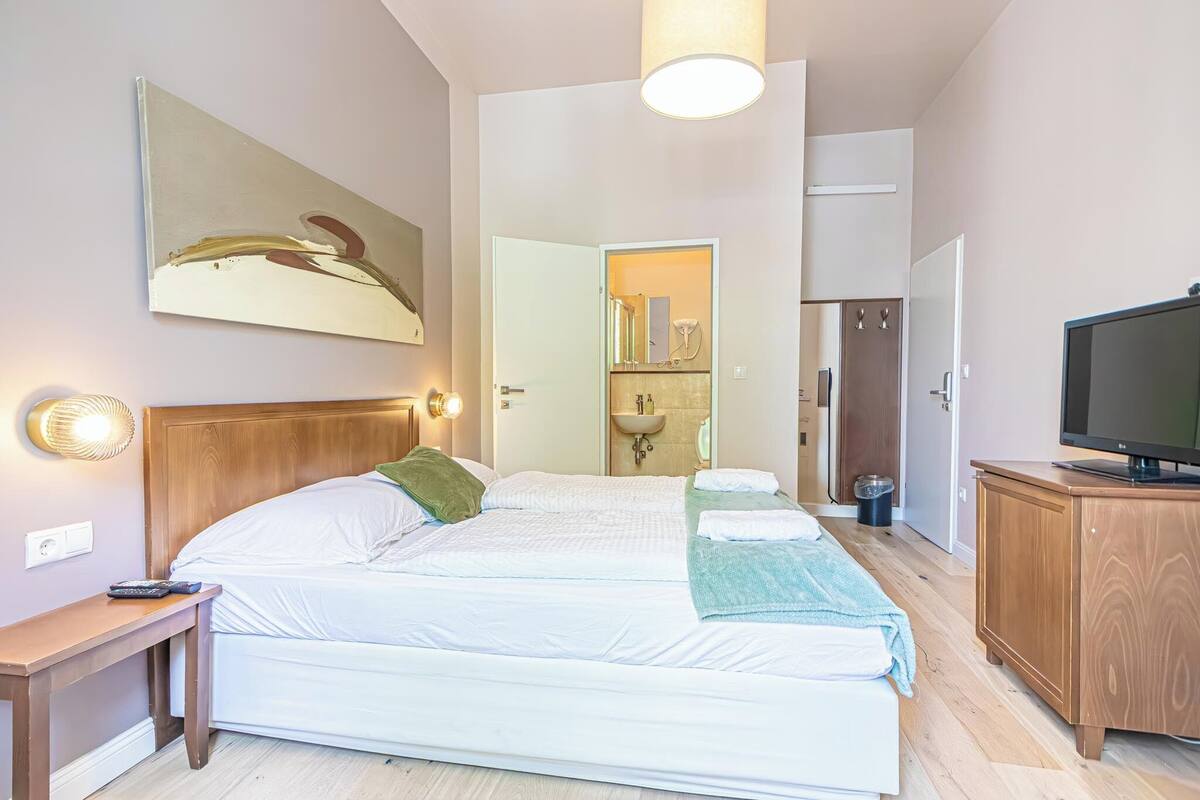 A bedroom with a large bed, bedside tables, a television, and a bathroom visible through an open door.