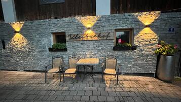 Un muro de piedra con un letrero que dice 'Kleebachhof' y el número '6' sobre un ventanal. Hay sillas de mimbre y una mesa adelante.